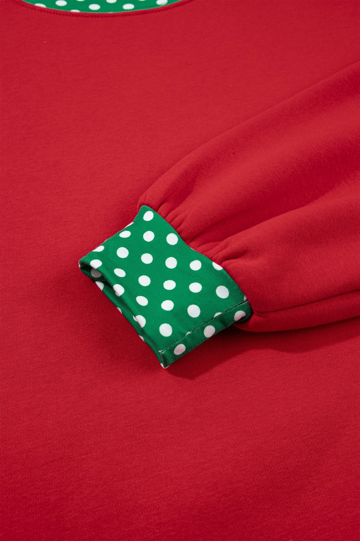 Close-up of a red garment with a green and white polka dot cuff detail.