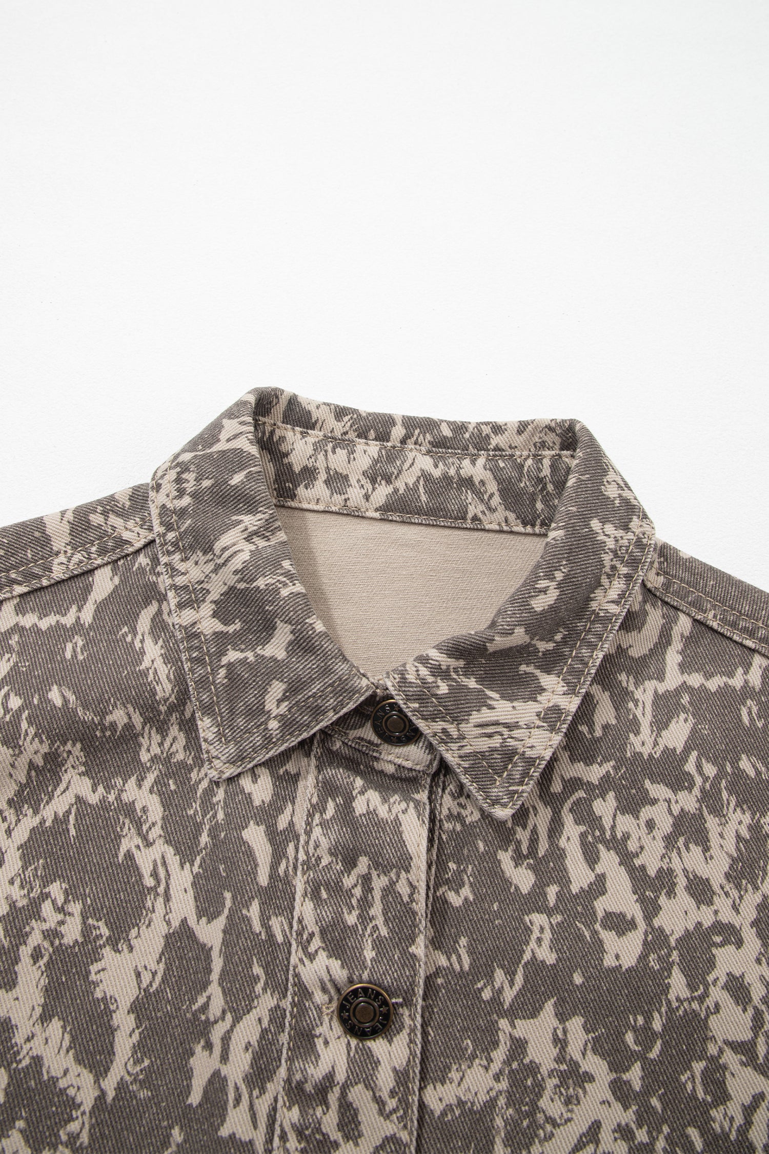 Close-up of collared button-front shirt with mottled gray and beige abstract pattern against light background.
