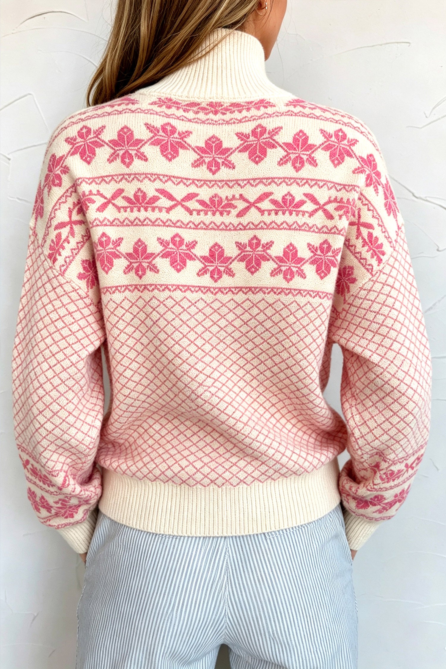 Person from behind in a cream Fair Isle sweater with pink patterns and light blue pinstriped pants.