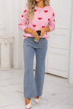 Person wearing a pink sweater with red heart patterns and blue jeans, holding a coffee cup.