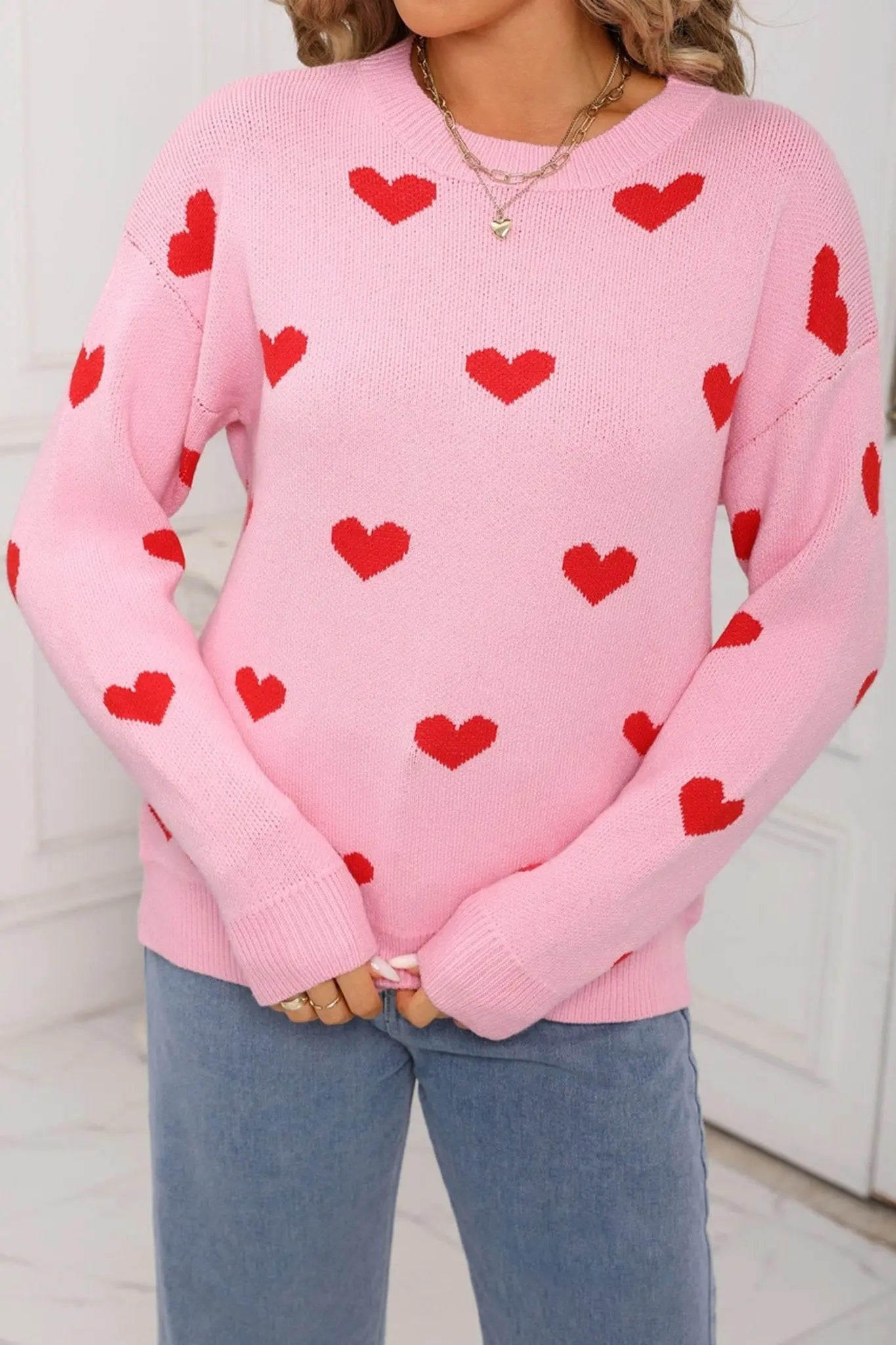 Person wearing a pink sweater with red heart patterns and blue jeans.