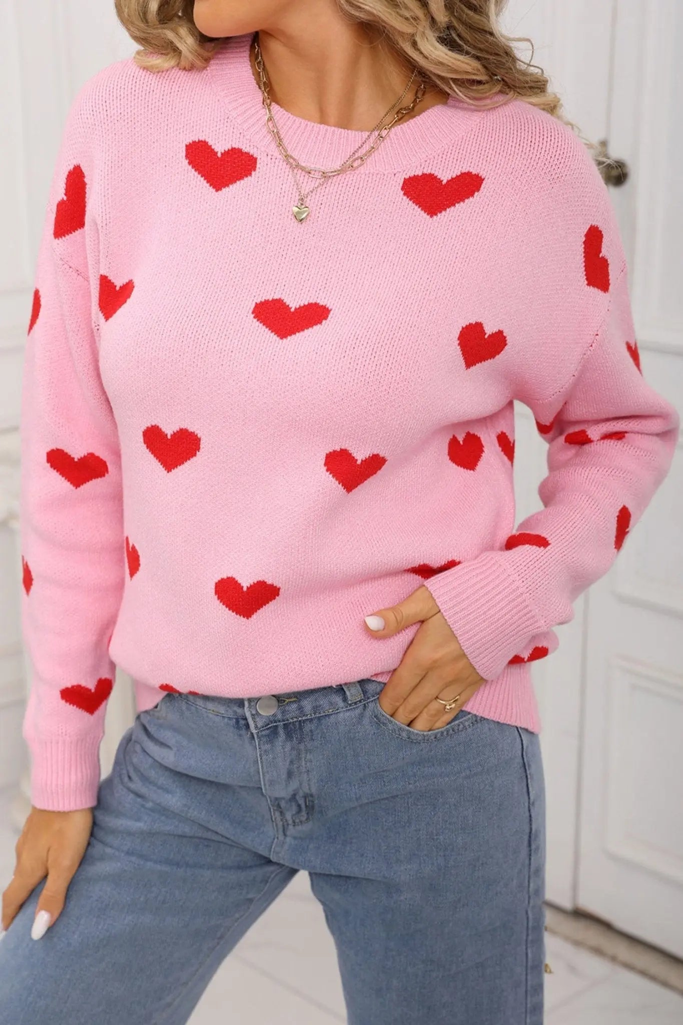 Person wearing a pink sweater with red heart patterns and blue jeans.