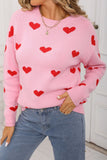 Person wearing a pink sweater with red heart patterns and blue jeans.