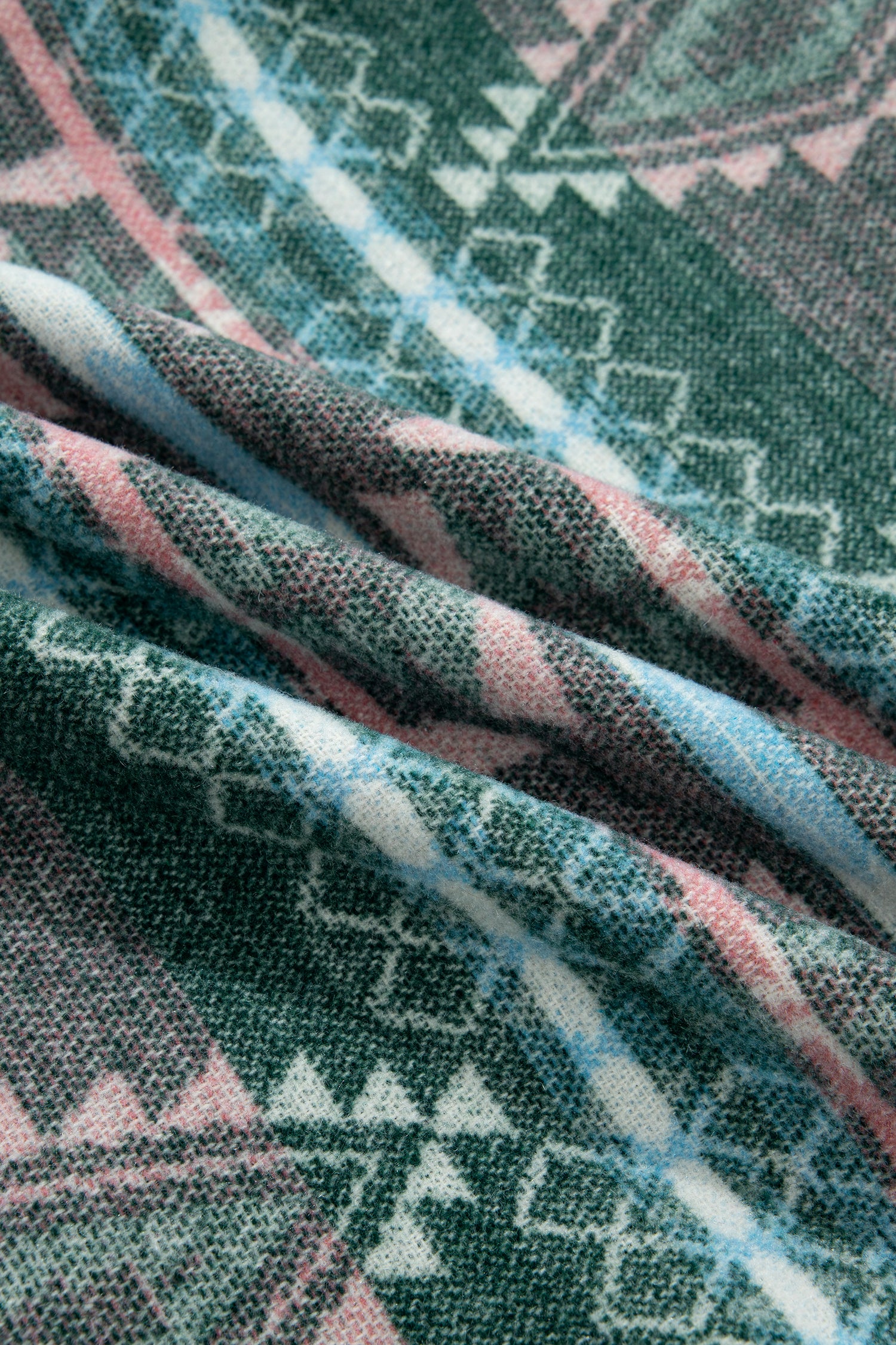 A close-up of a woven textile with a geometric pattern in dark green, pink, light blue, and white, shown with soft folds.