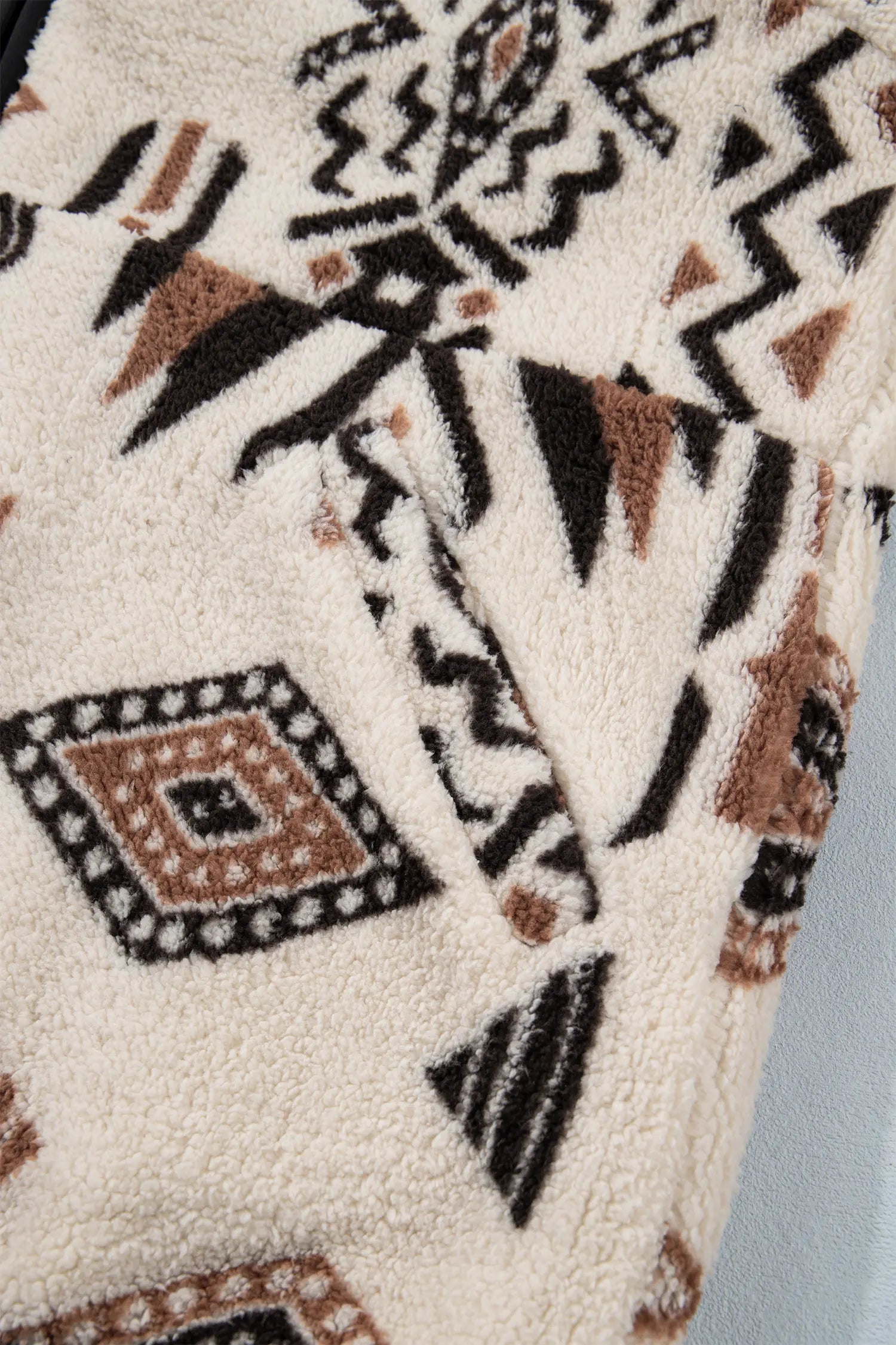 Close-up of a textured sherpa fleece fabric with a Southwestern geometric pattern in black, brown, and beige.