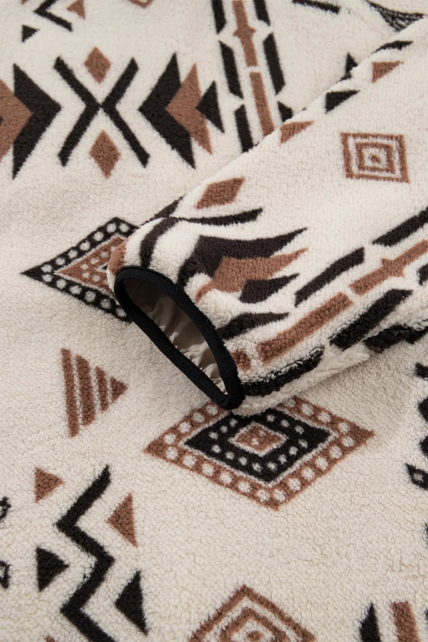 A close-up of a fleece blanket with a Southwestern geometric pattern in black, brown, and cream.