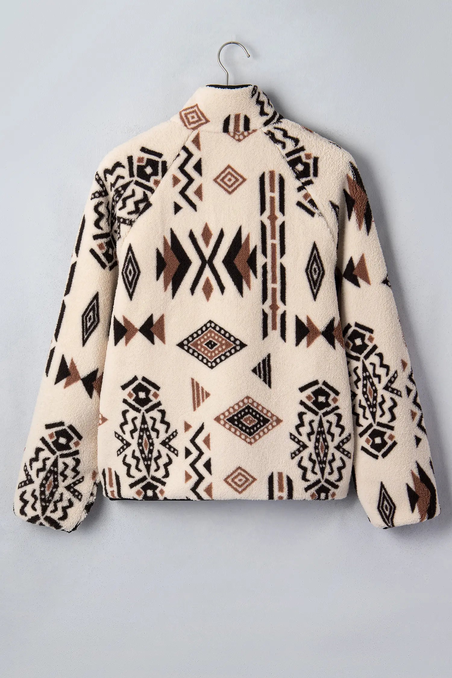 A fleece jacket with a Southwestern geometric pattern in black, brown, and cream, hanging on a metal hanger against a light gray background.