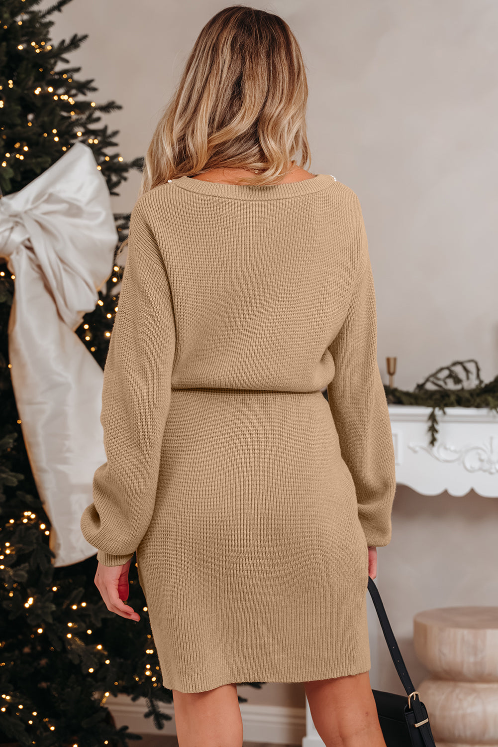 Woman wearing a beige ribbed dress in a festive setting with a decorated Christmas tree and fireplace.