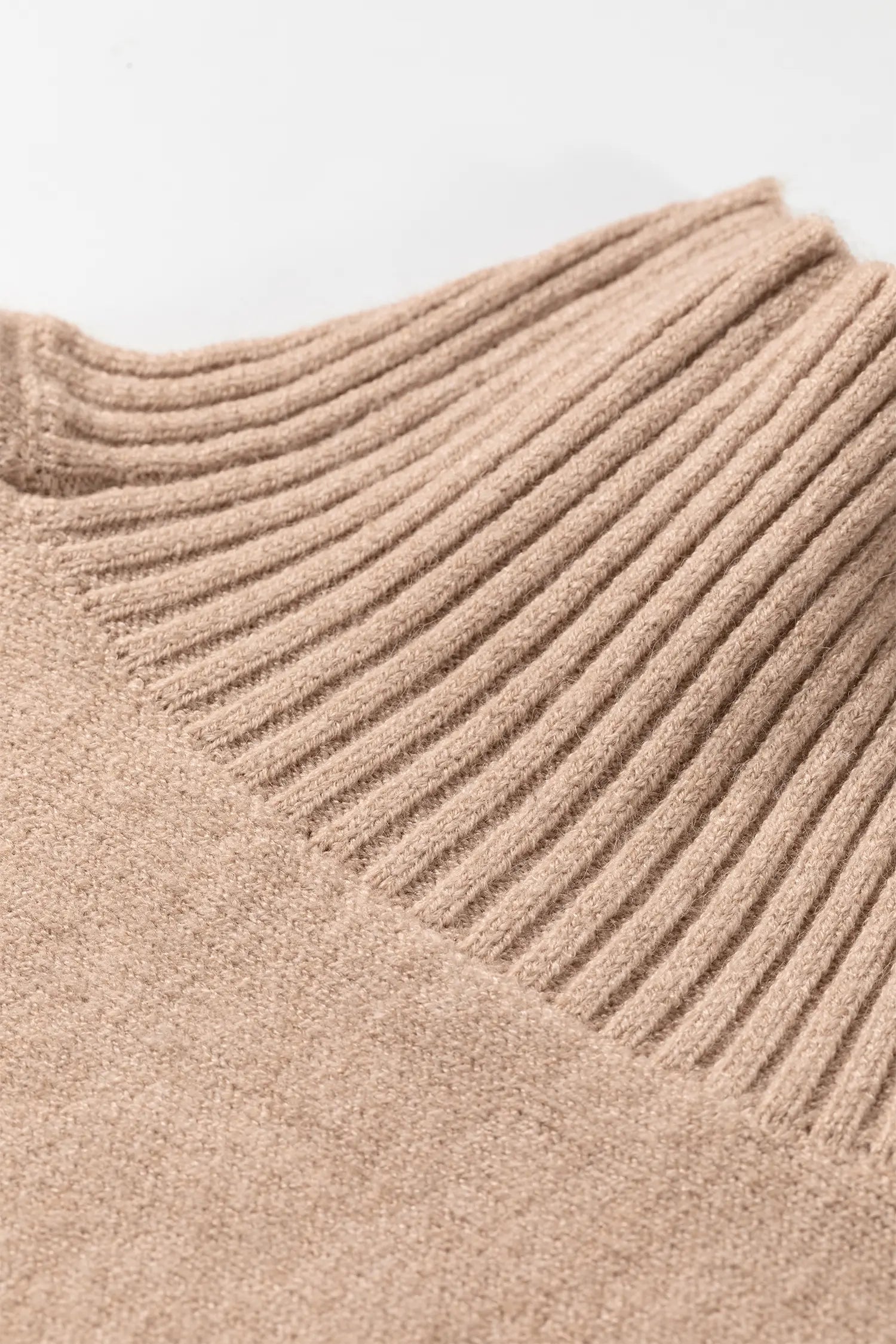 Close-up of warm beige ribbed knit sweater featuring textured fabric and detailed collar.