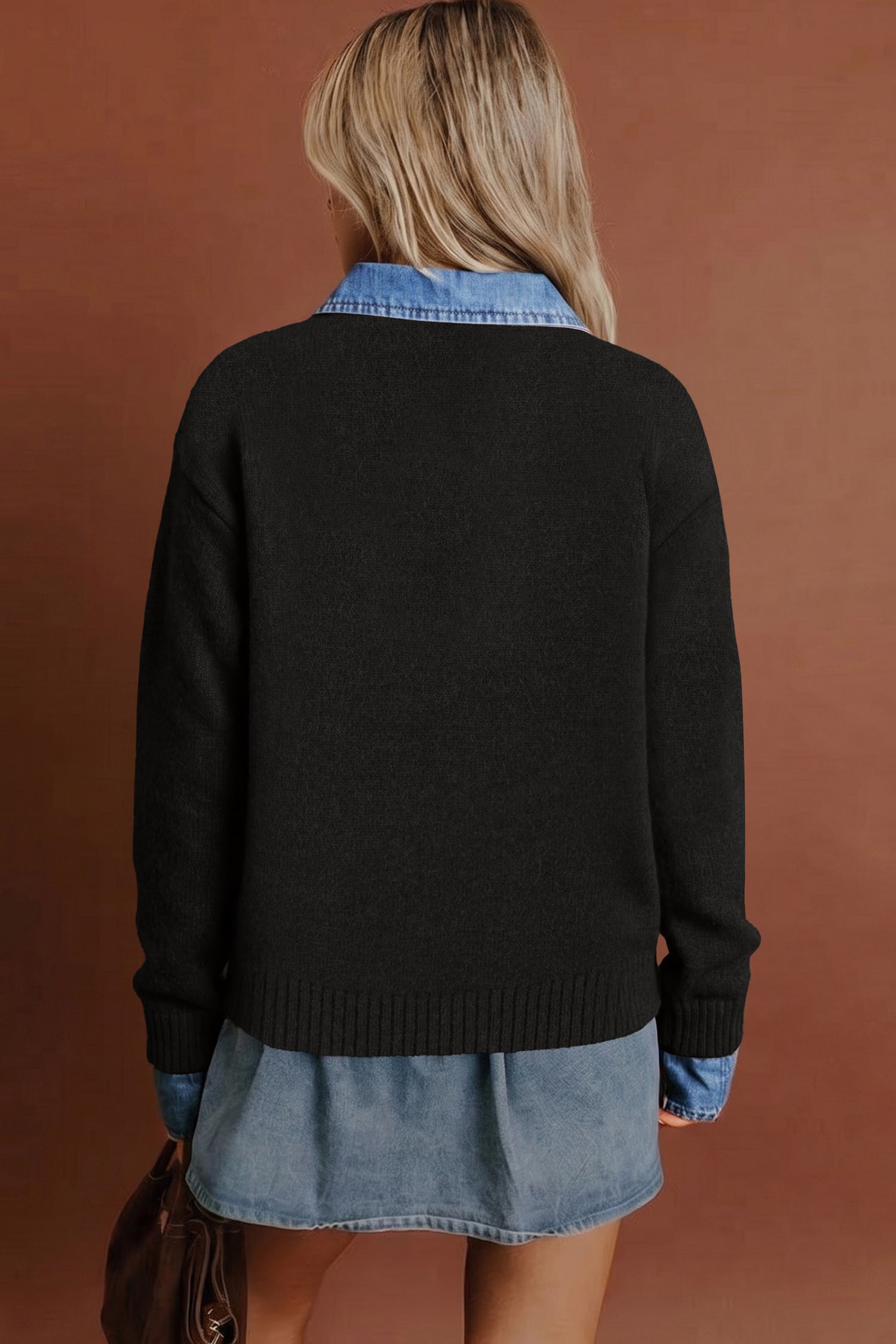 A woman shown from the back wearing a black knit sweater layered over a light blue denim shirt and denim skirt, against a solid warm brown background.