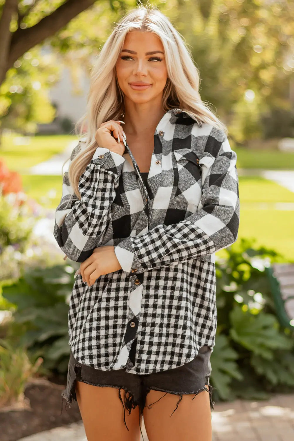 Woman wearing a black and white checkered shirt outdoors with greenery in the background