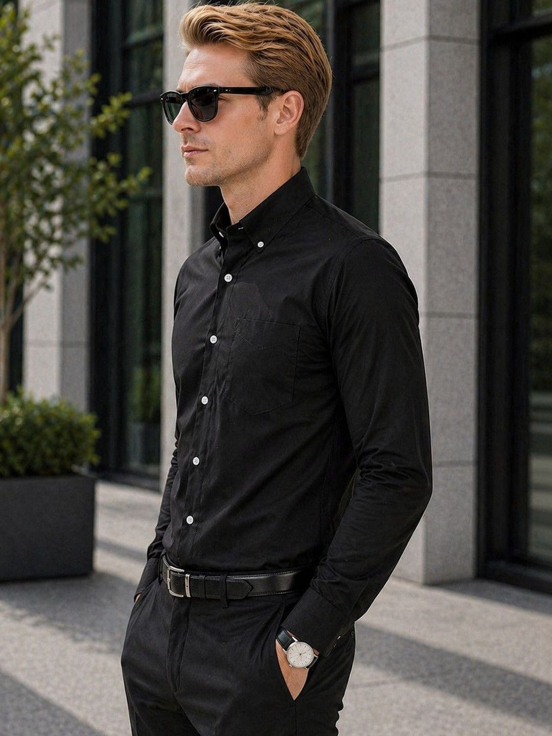 Man wearing a black shirt and sunglasses standing outdoors.