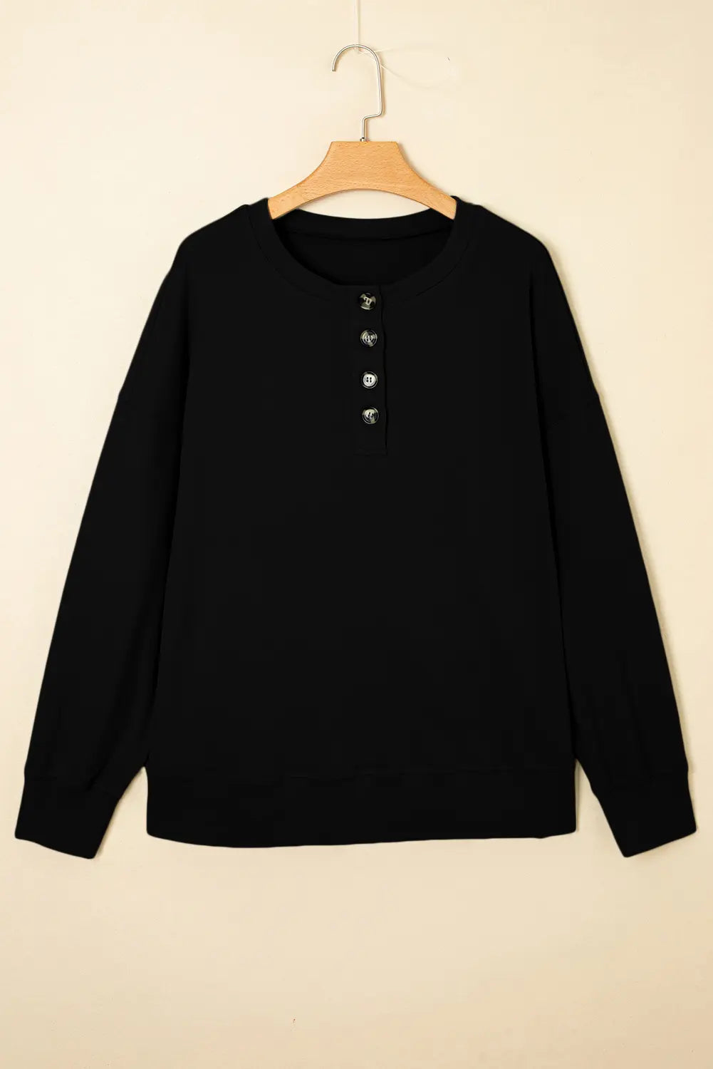 A black long-sleeve henley sweatshirt hanging on a wooden hanger against a plain beige wall.