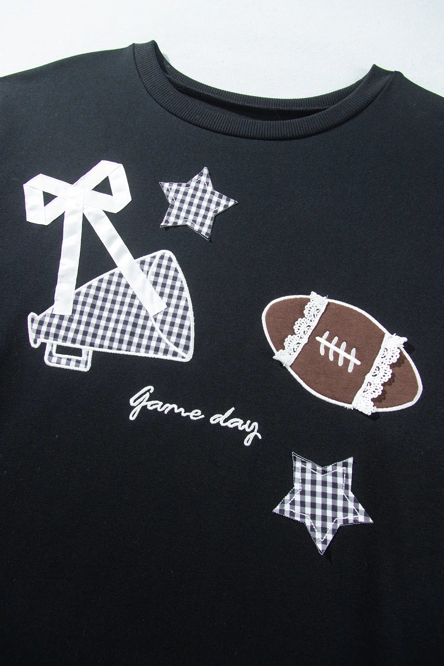 Close-up of a black “Game Day” football tee with a gingham megaphone, football, and stars.