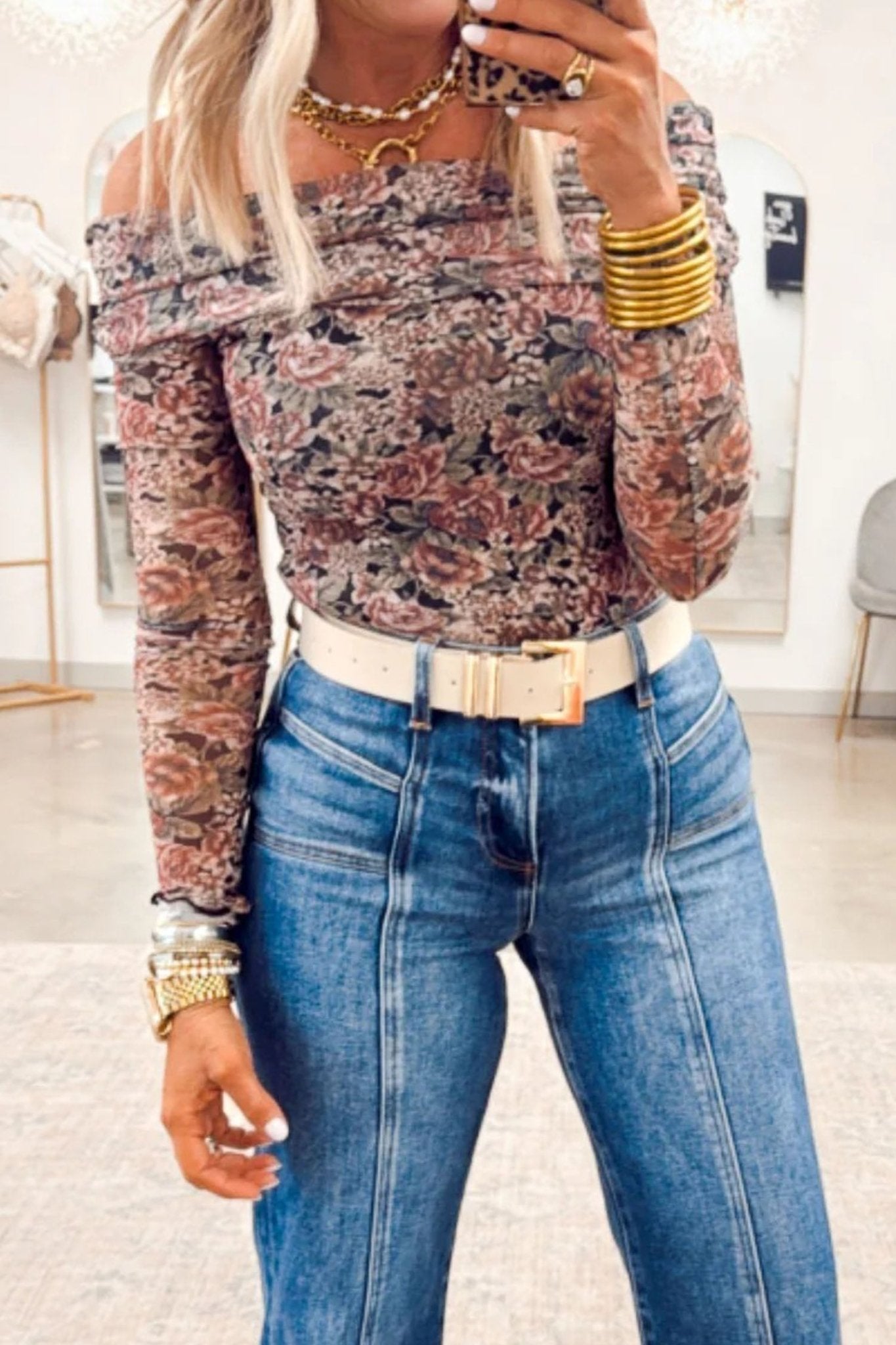 Person wearing a floral off-shoulder top and blue jeans indoors.