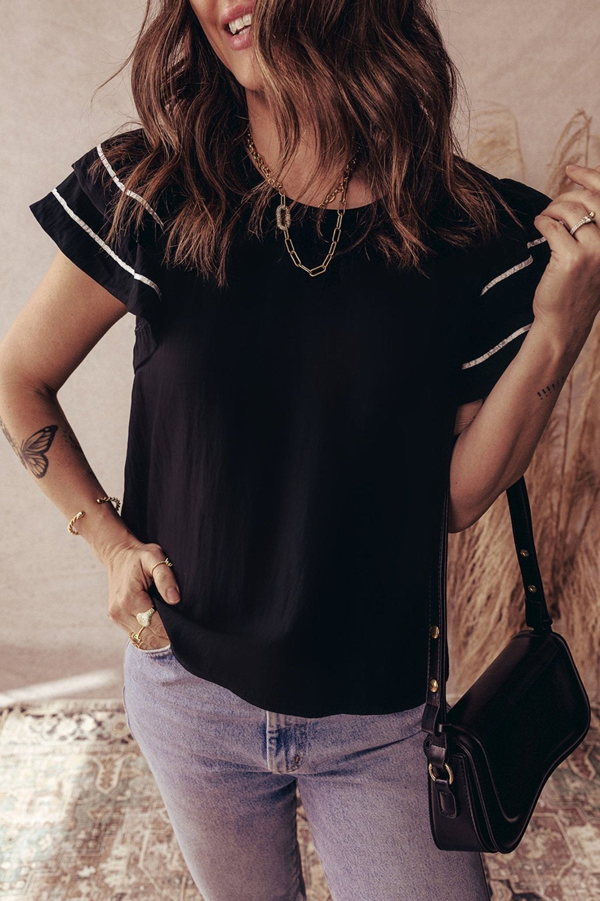 Woman wearing a black top with white trim and light blue jeans, holding a black handbag.