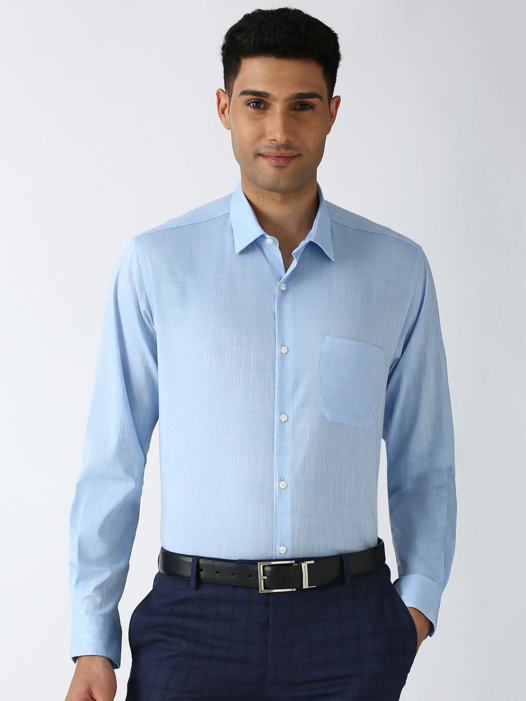 Man wearing a light blue dress shirt and dark pants on a white background