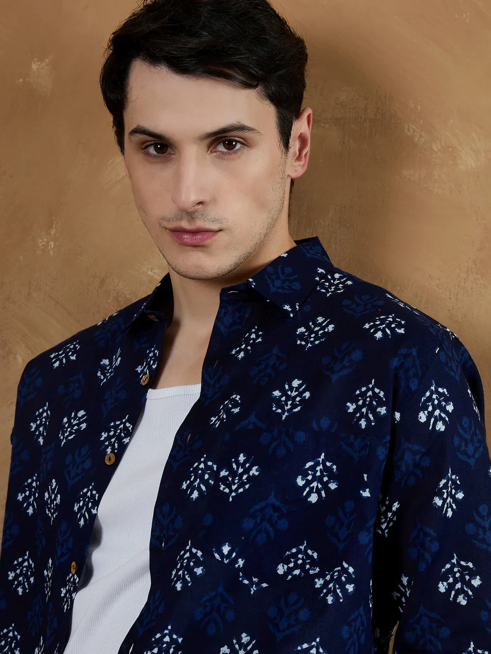 Man wearing a dark blue patterned shirt over a white shirt against a beige background