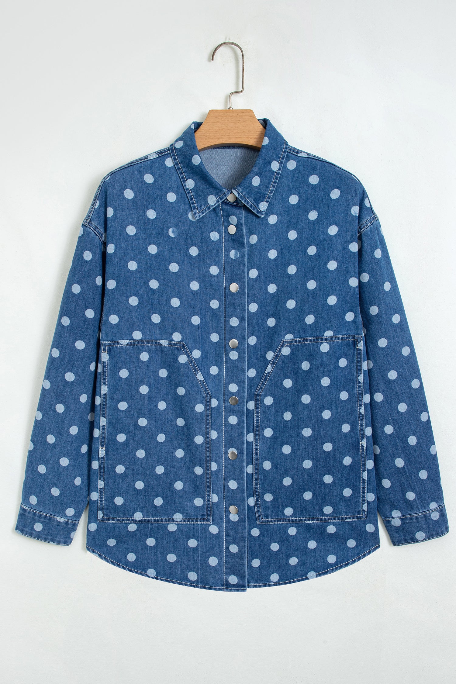 Blue denim shirt jacket with white polka dots hanging on a wooden hanger against a white background.