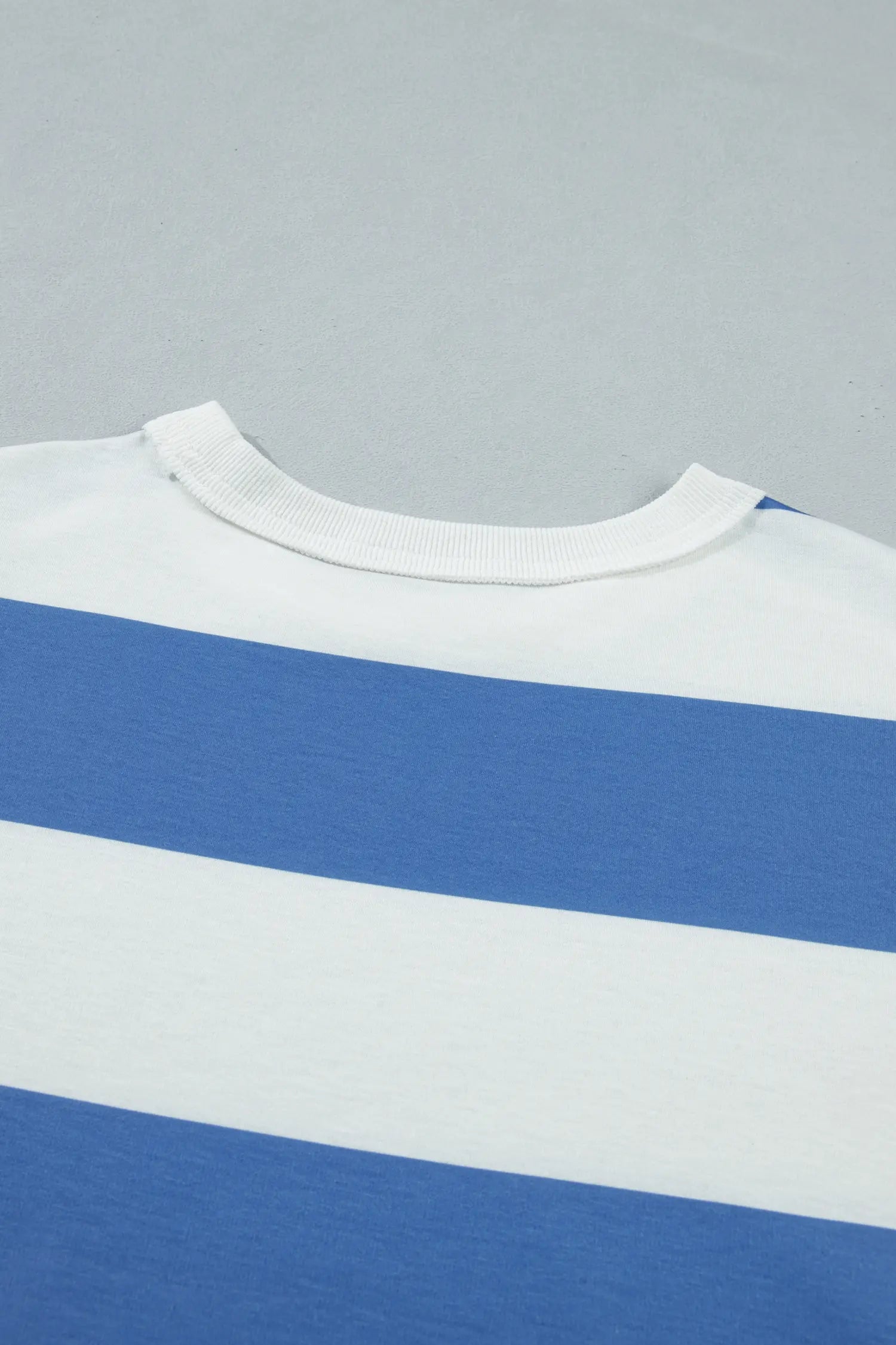 Close-up of a striped t-shirt showing a white crew neck collar, white fabric, and a medium blue stripe, set against a solid gray background.