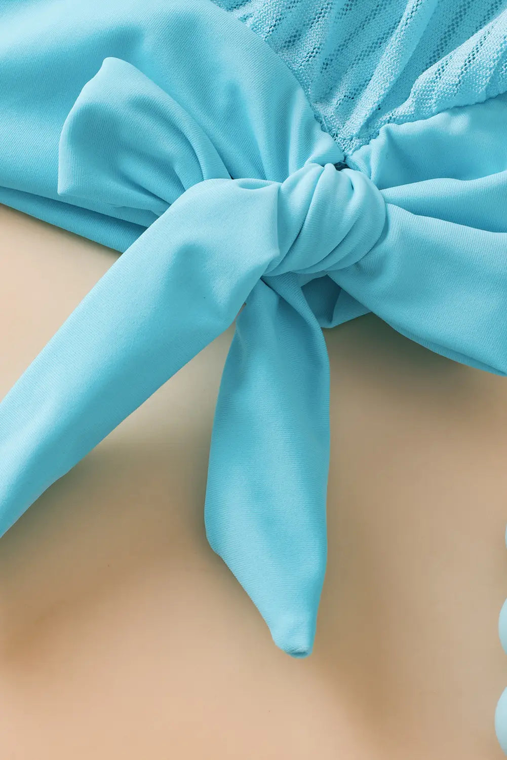 Close-up of a blue bikini top with a knot detail on a beige background