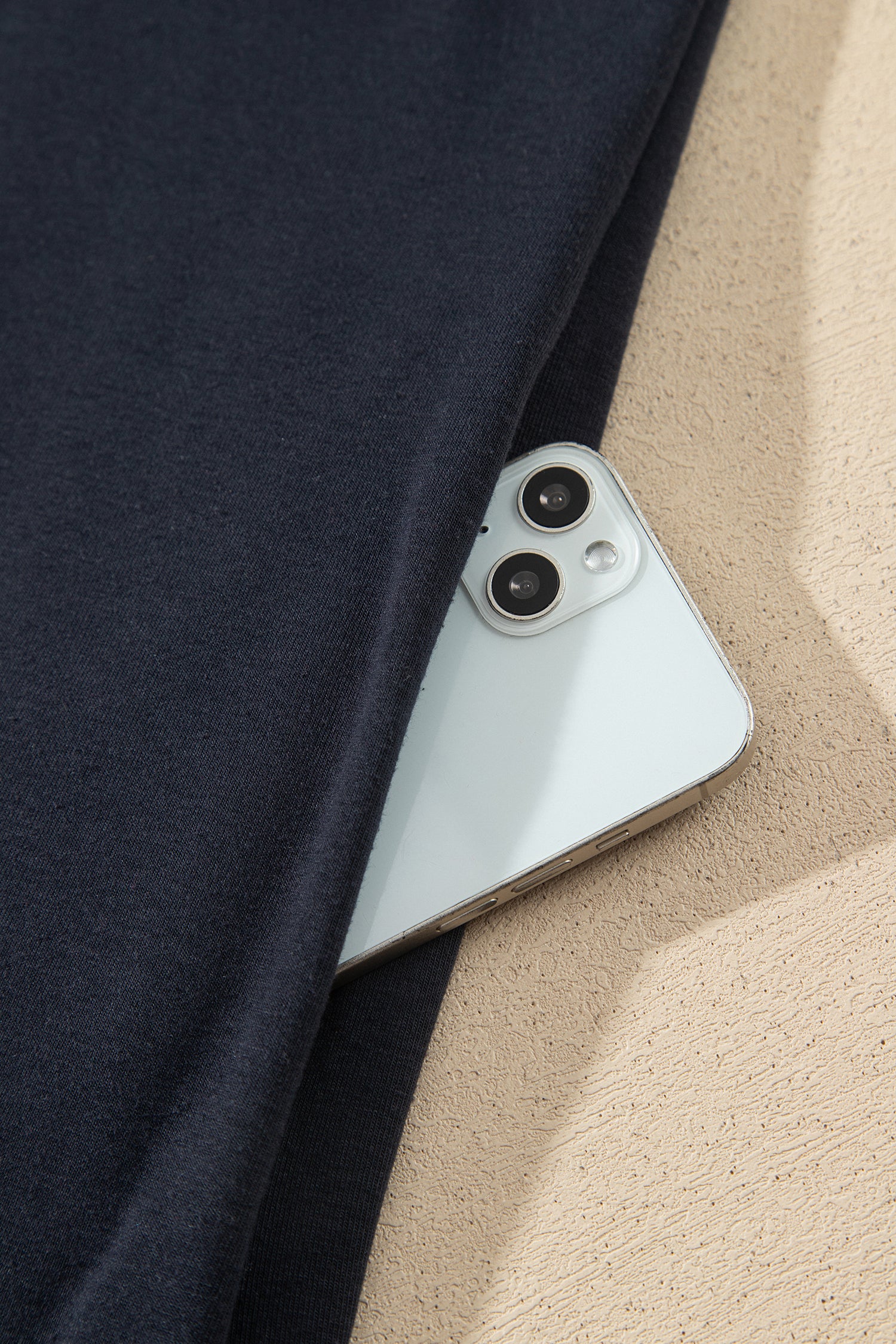 A close-up of a light silver smartphone partially tucked under a dark navy fabric, 