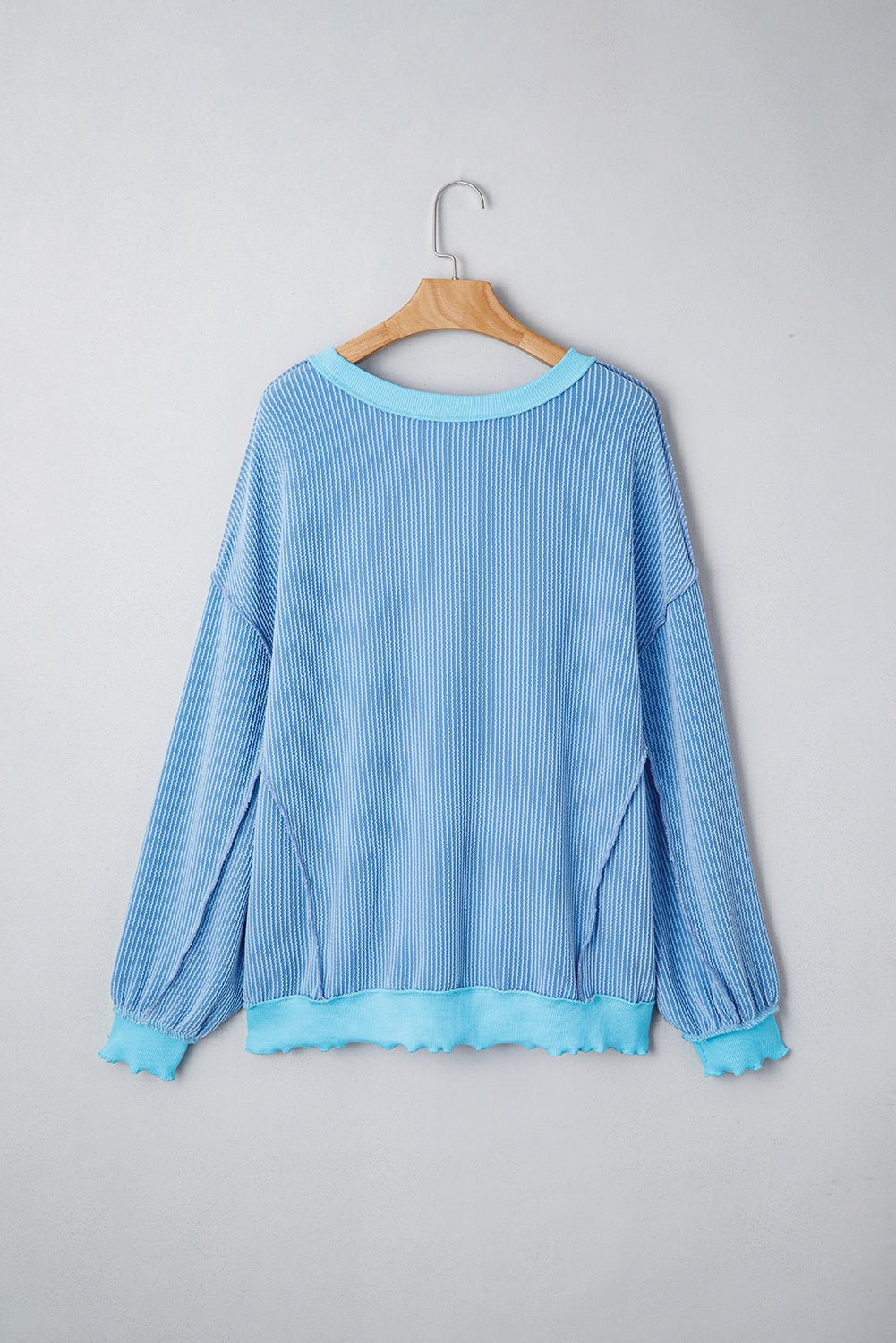 Blue ribbed sweater on a wooden hanger against a gray background