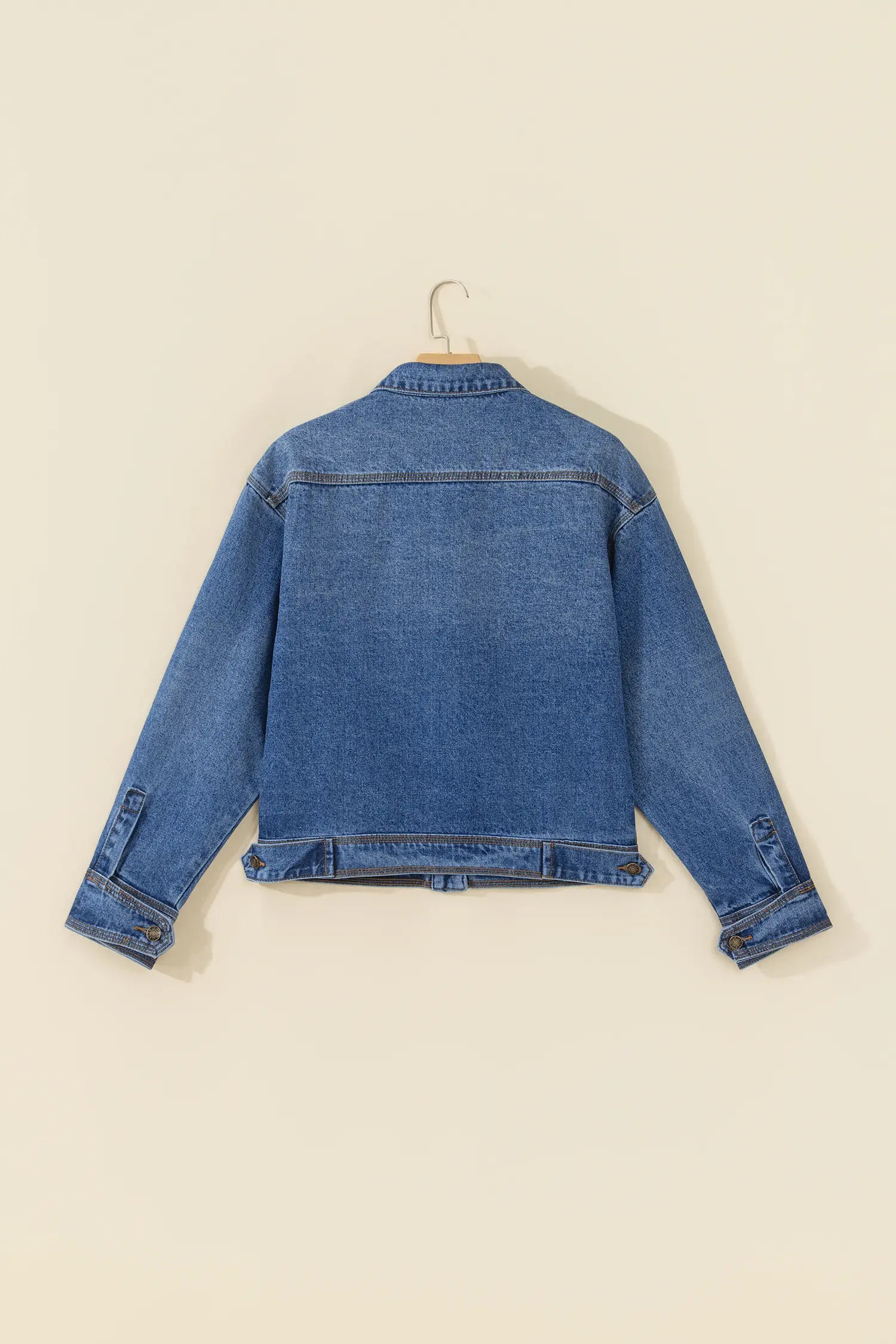 A blue denim jacket shown from the back, hanging on a wooden hanger