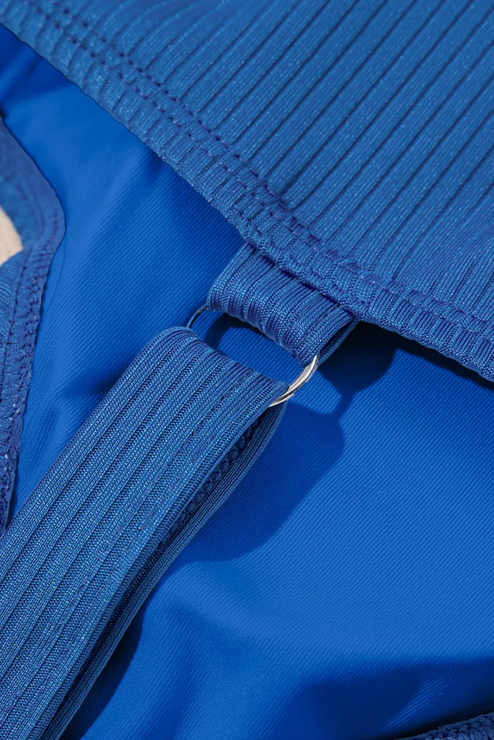 Close-up detail of a bright blue ribbed fabric garment, showing the texture of the straps and a metal ring connector.