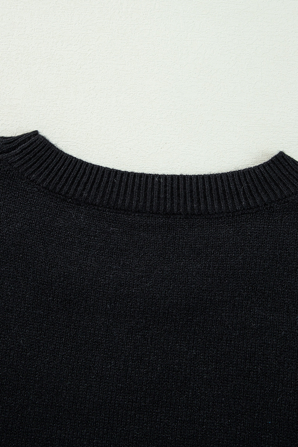 Close-up of a black ribbed knit sweater or shirt collar against a plain off-white background.