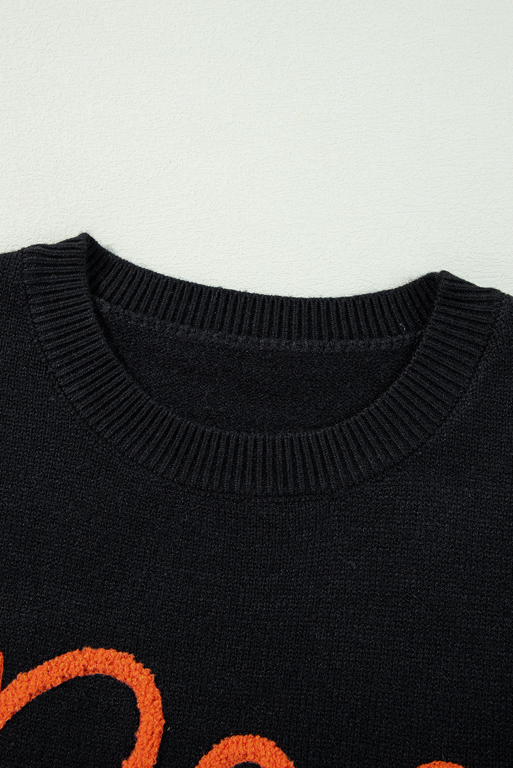Close-up of a black sweater with orange text on a light gray background