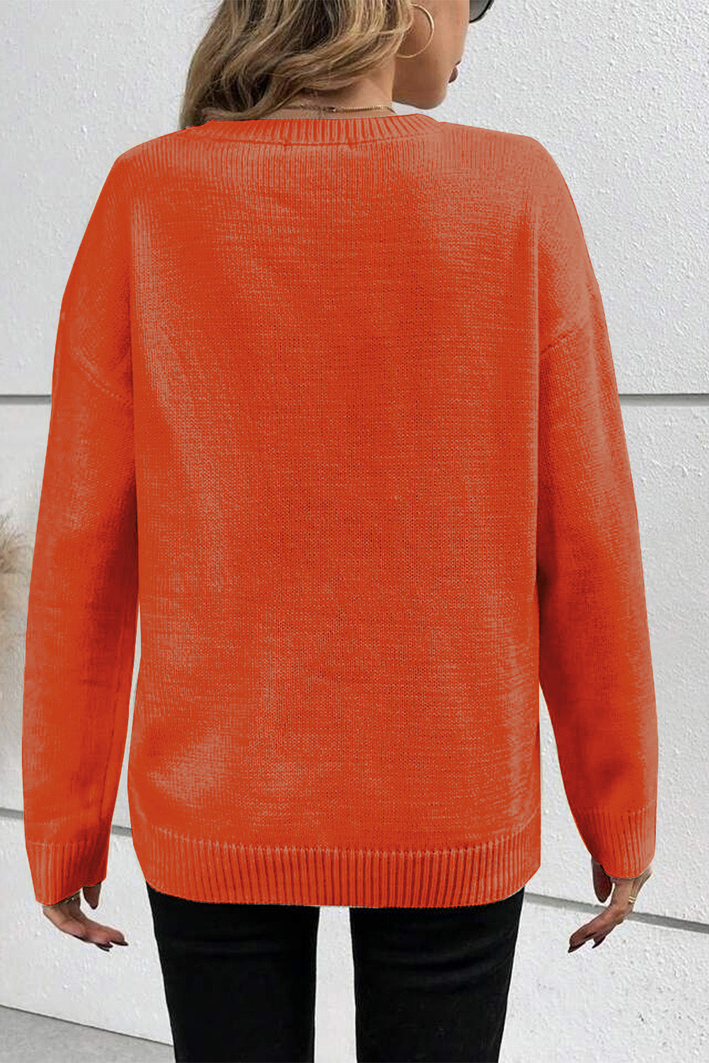Person wearing an orange sweater against a white wall
