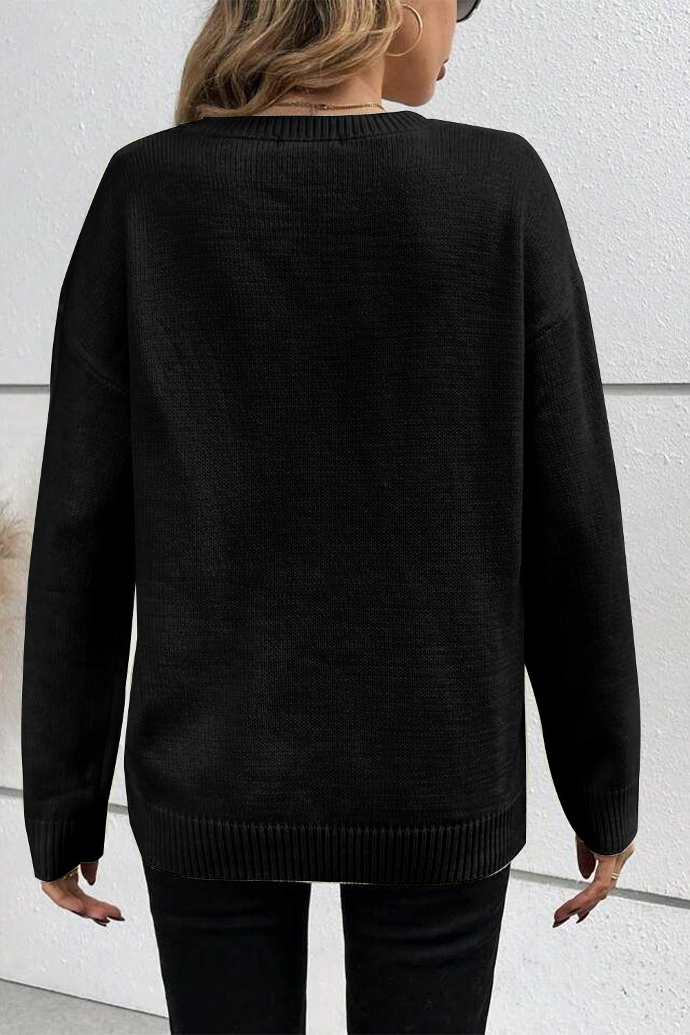 Person wearing a black sweater against a white wall