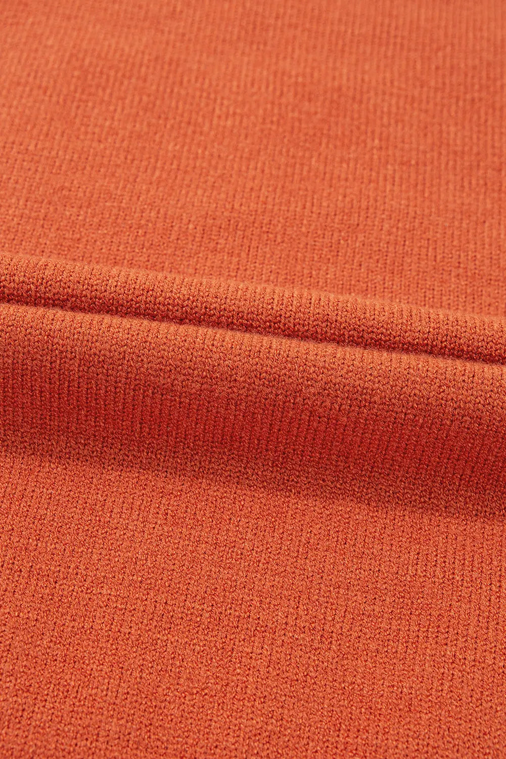 Close-up of a textured knit fabric in a warm rust-orange color, showing the ribbed weave and a folded seam.