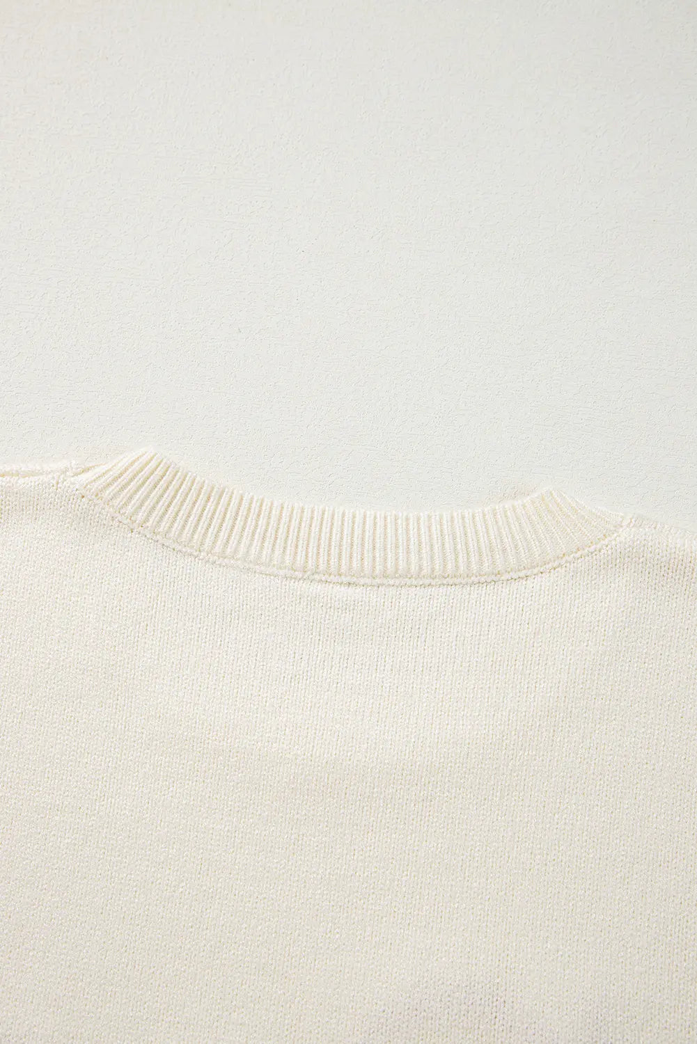 Close-up of cream knit garment with ribbed crew neck collar.