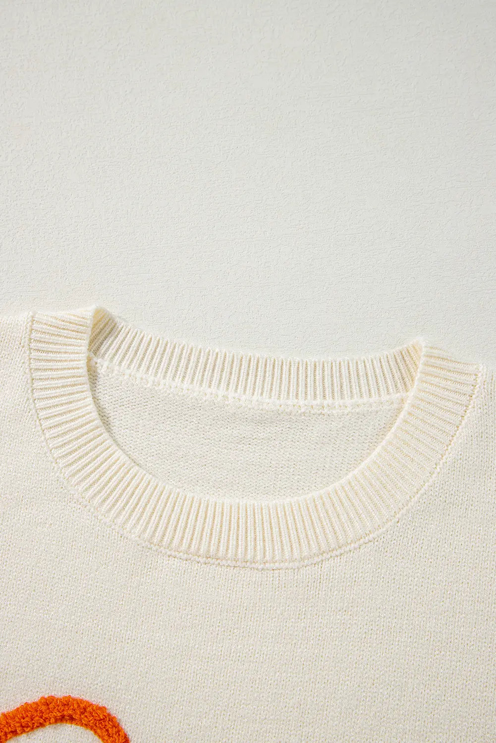 Close-up of cream knit sweater with ribbed crew neck and orange graphic detail.