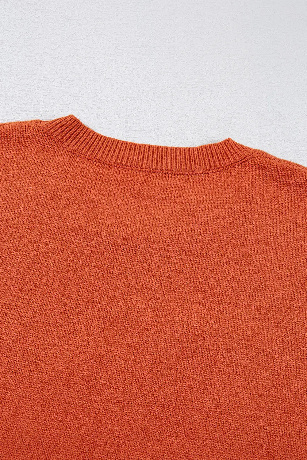 Close-up of warm rust-orange ribbed crewneck sweater showing knit texture.
