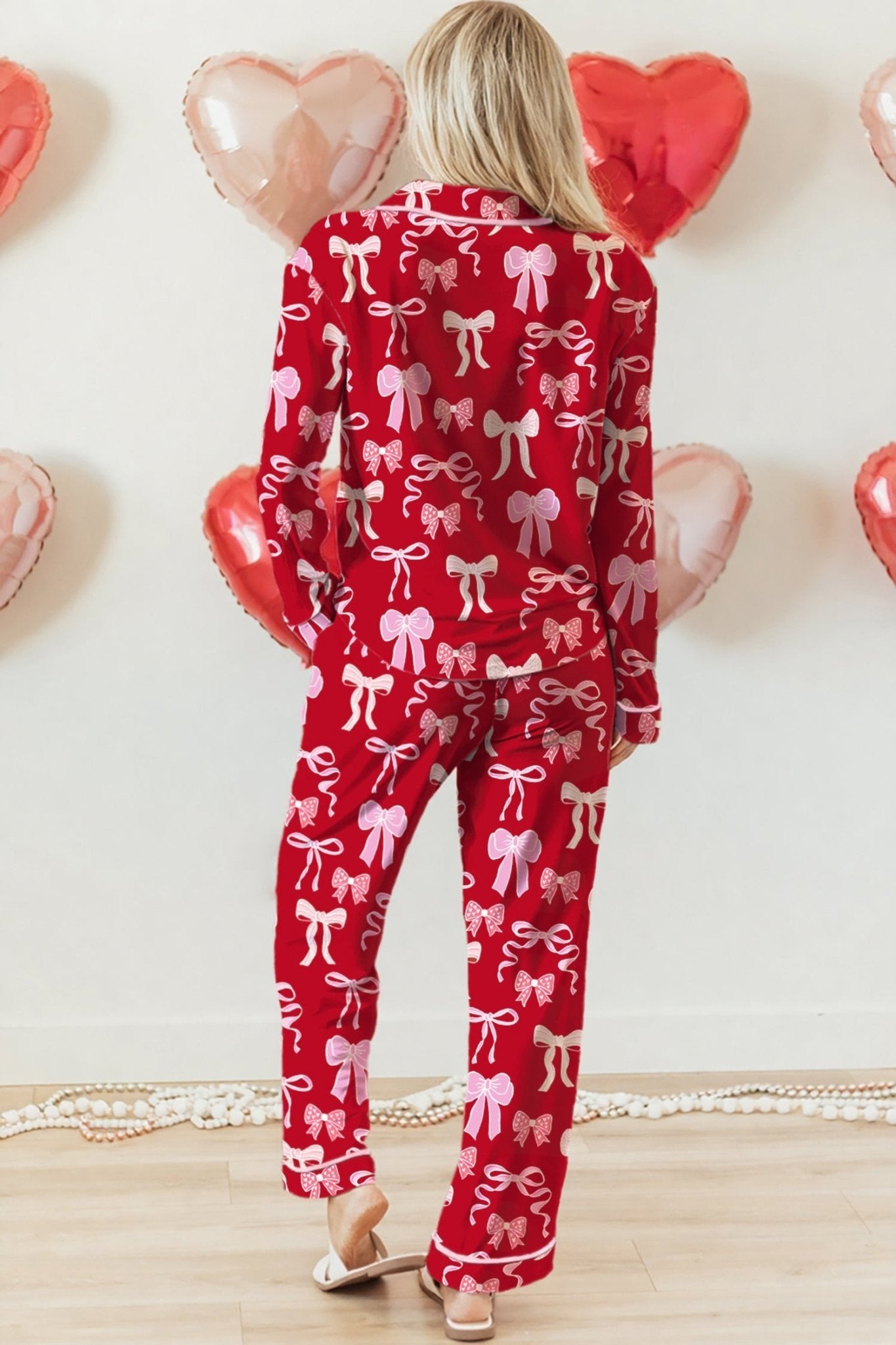 Person wearing a red outfit with pink bows in front of heart-shaped balloons.