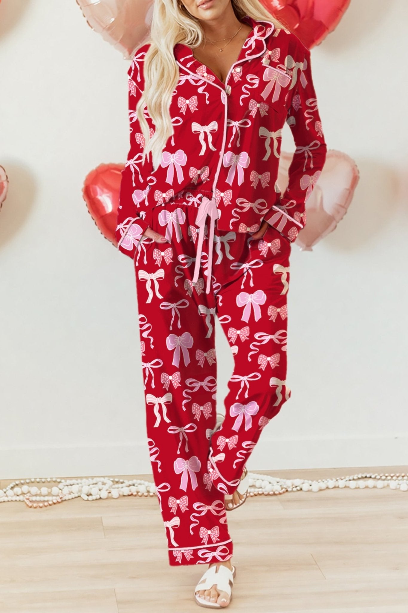Person wearing a red outfit with pink bows, holding heart-shaped balloons on a light background.