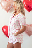 Woman wearing a pink and white pajama set with heart-shaped balloons in the background.