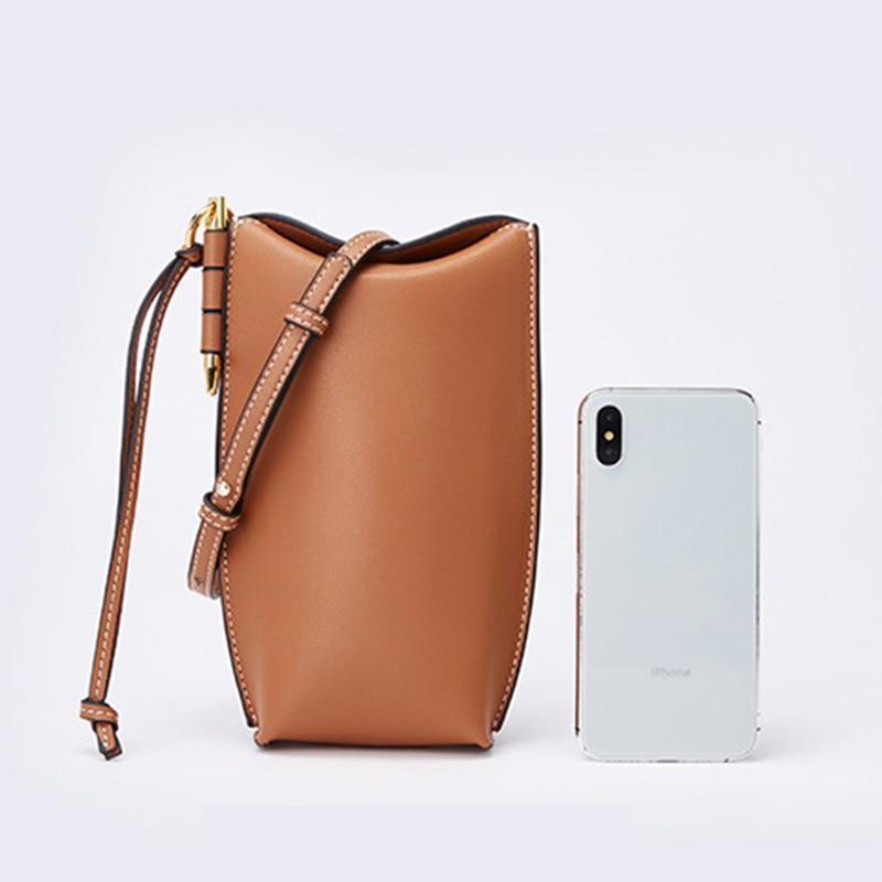 Brown leather bucket bag next to a smartphone on a light gray background