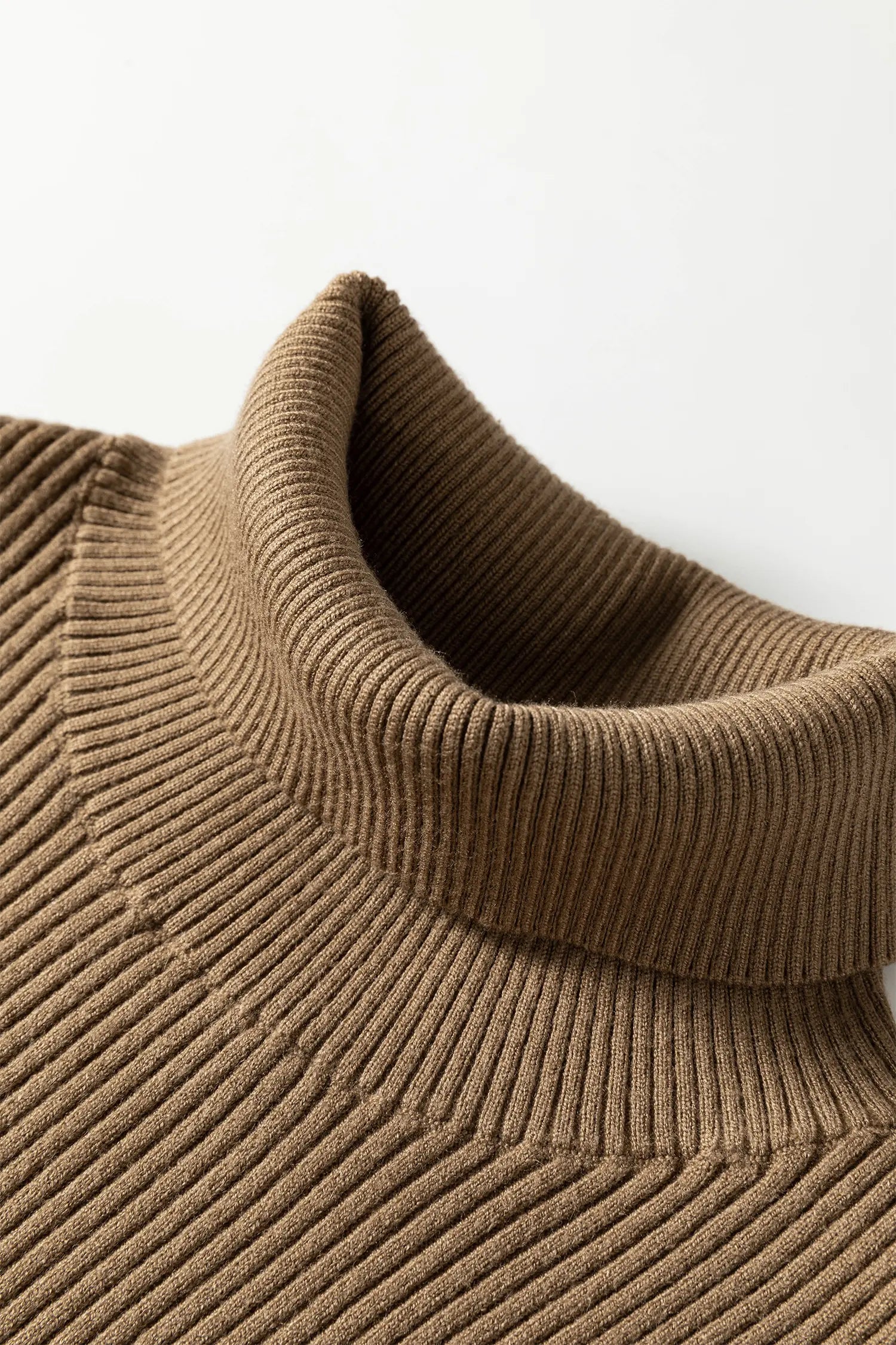 Close-up of a ribbed knit turtleneck sweater in a warm taupe-brown color, showing the texture and collar detail against a light gray background.