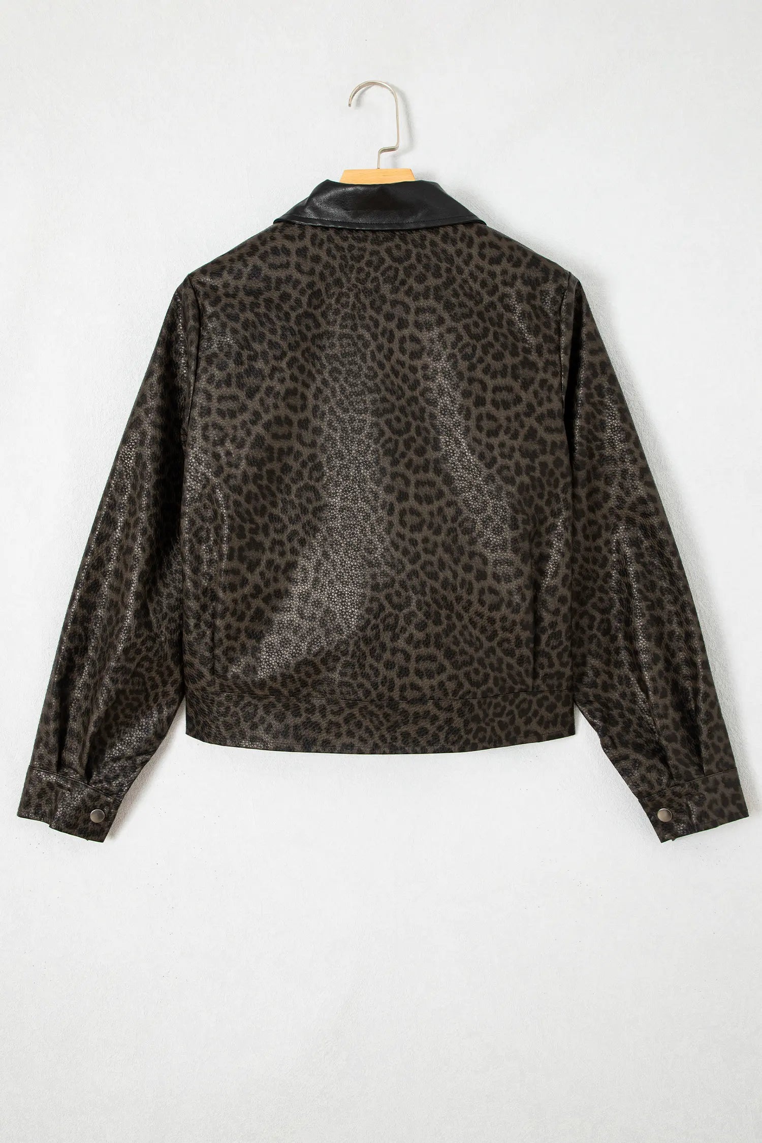 A cropped long-sleeve jacket with a brown and black leopard print pattern, featuring a contrasting black collar, hanging on a wooden hanger against a plain white background.