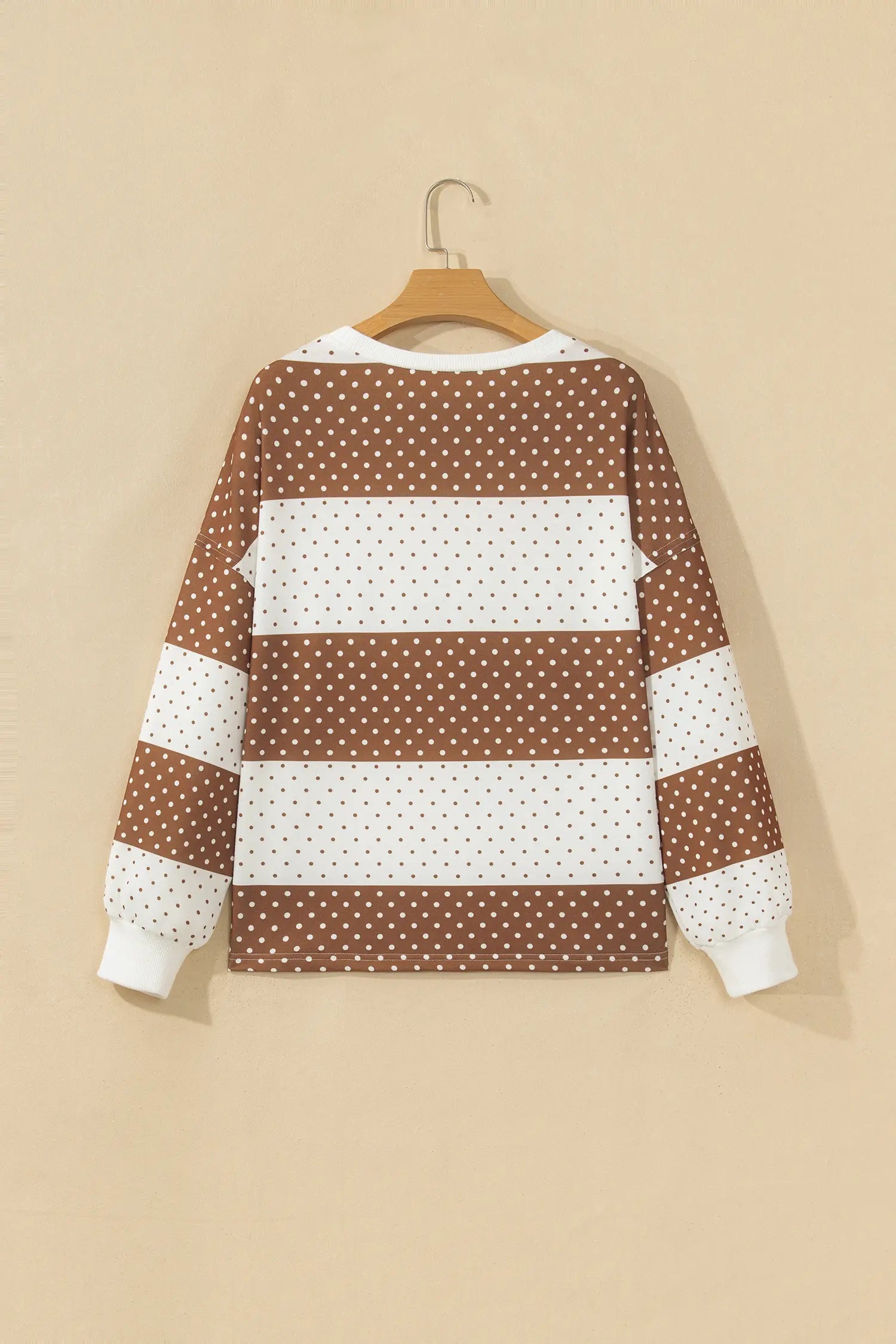 Brown and white striped long-sleeve top with polka dots on a wooden hanger.
