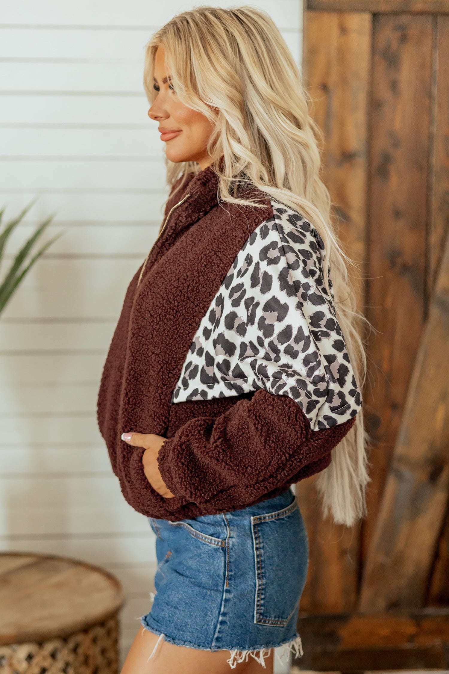 Woman in brown sherpa fleece jacket with leopard-print sleeves and denim shorts.