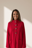 Woman wearing a red coat with silver buttons against a beige background