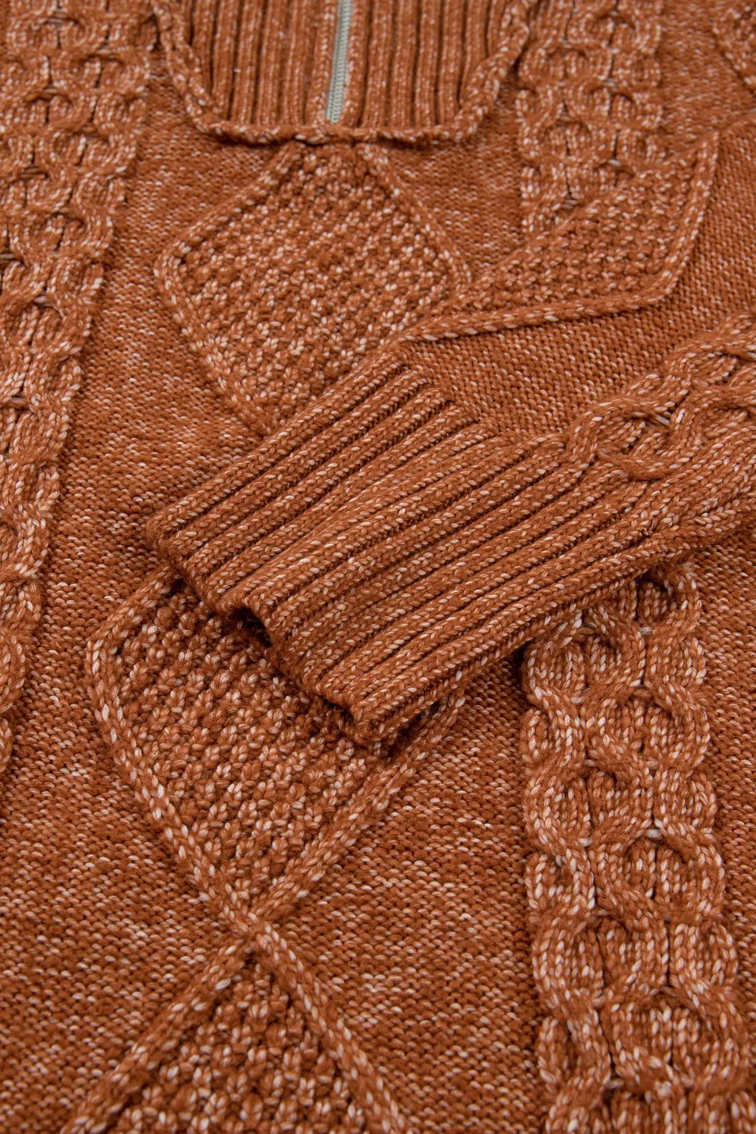 Close-up of a textured knit sweater in a warm rust brown color, showing detailed cable and ribbed patterns.