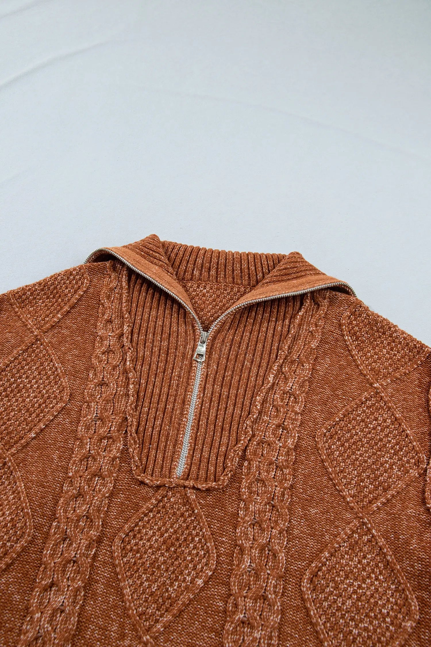 Close-up of brown quarter-zip cable-knit sweater with detailed diamond patterns on light gray.