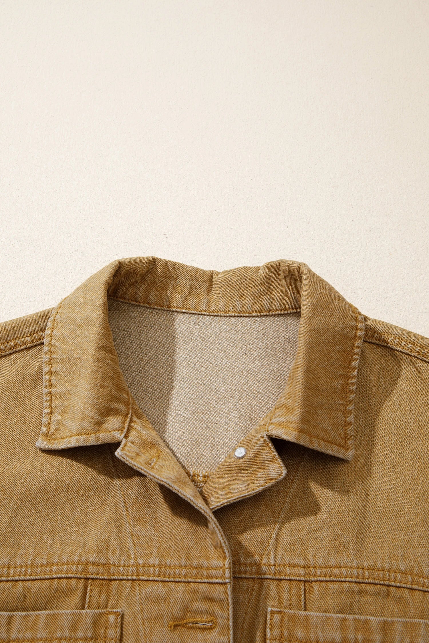 Close-up of a tan canvas utility jacket collar with a button closure, set against a plain off-white background.