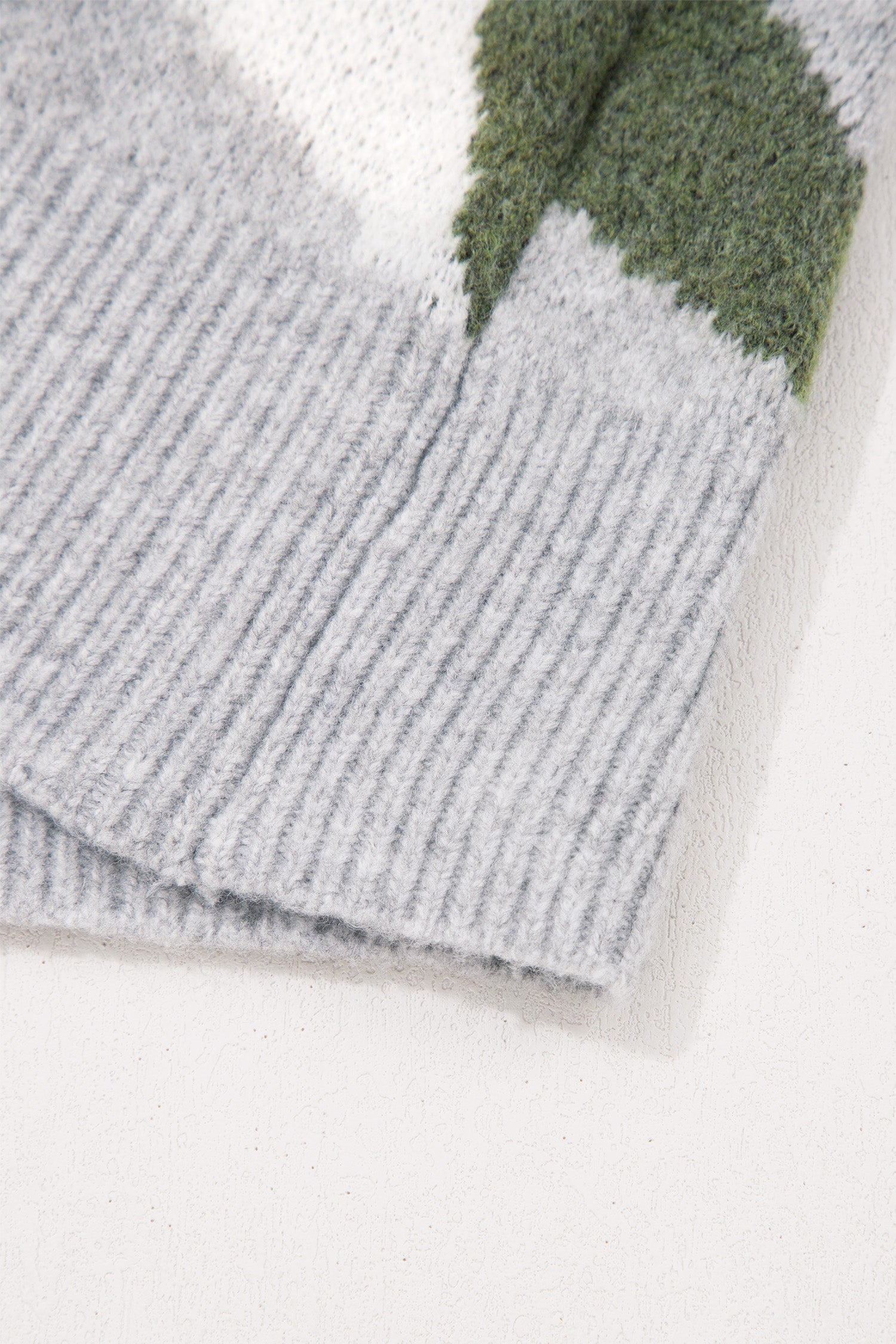Close-up of a ribbed knit fabric in light gray with a green and white patterned section.